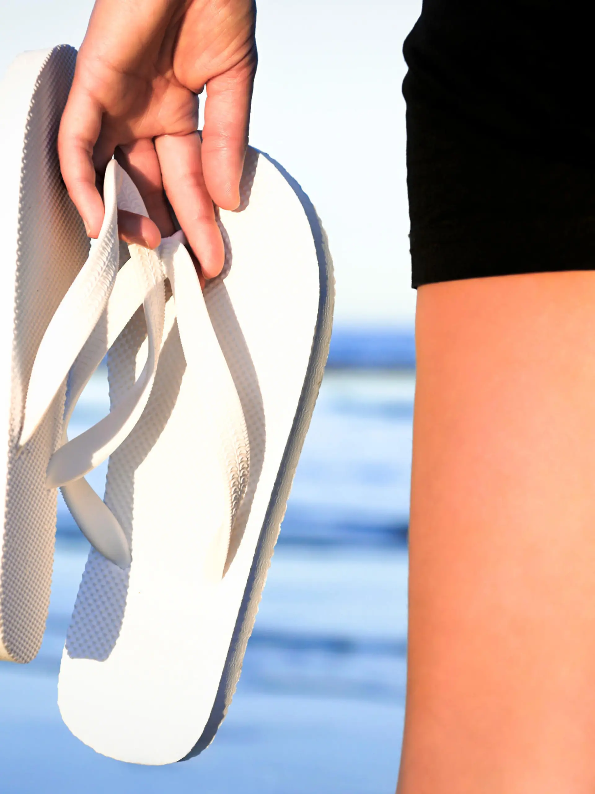 Frau trägt Flip-Flops in der Hand am Strand