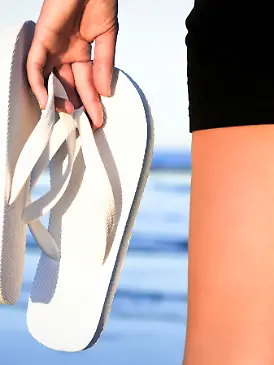 Frau trägt Flip-Flops in der Hand am Strand