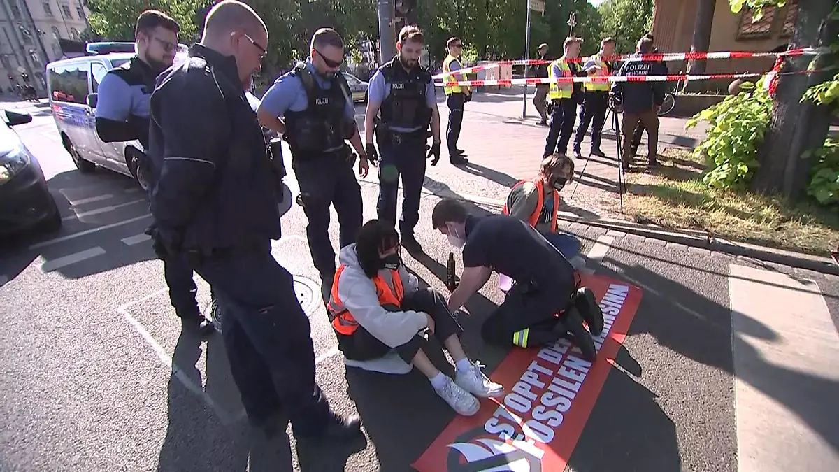 09.05.2022, Sachsen, Leipzig: Umweltaktivisten der Gruppe ·Letzte Generation· haben sich auf der Fahrbahn fest geklebt und ein Polizist versucht den Kleber zu lösen. Einsatzkräfte der Polizei sperrten den Bereich ab und entfernten die Demonstranten. Der Verkehr staute sich weiträumig. Foto: Tobias Junghannß/TNN/dpa +++ dpa-Bildfunk +++