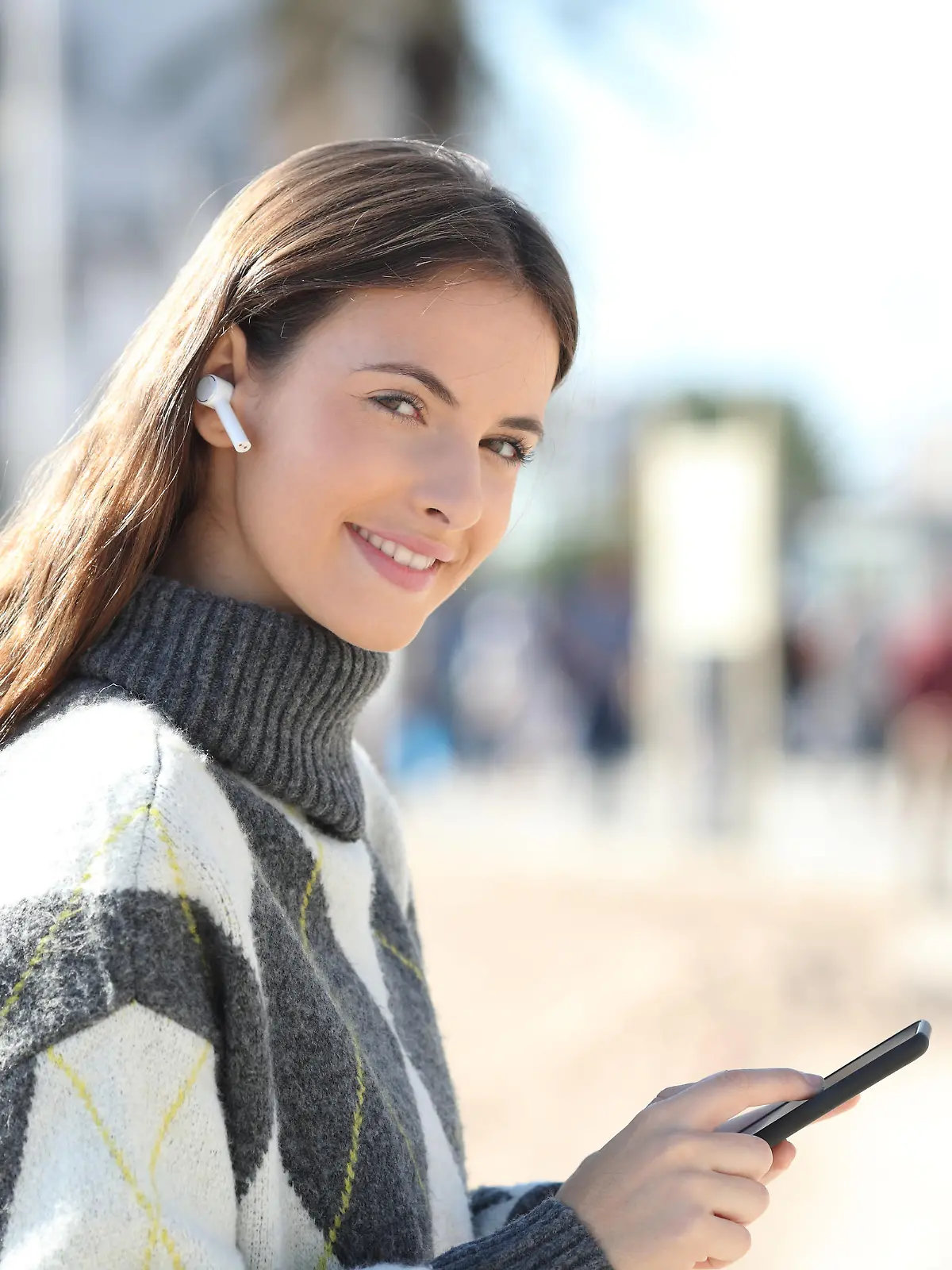 Happy girl holds phone listening to music looking at camera