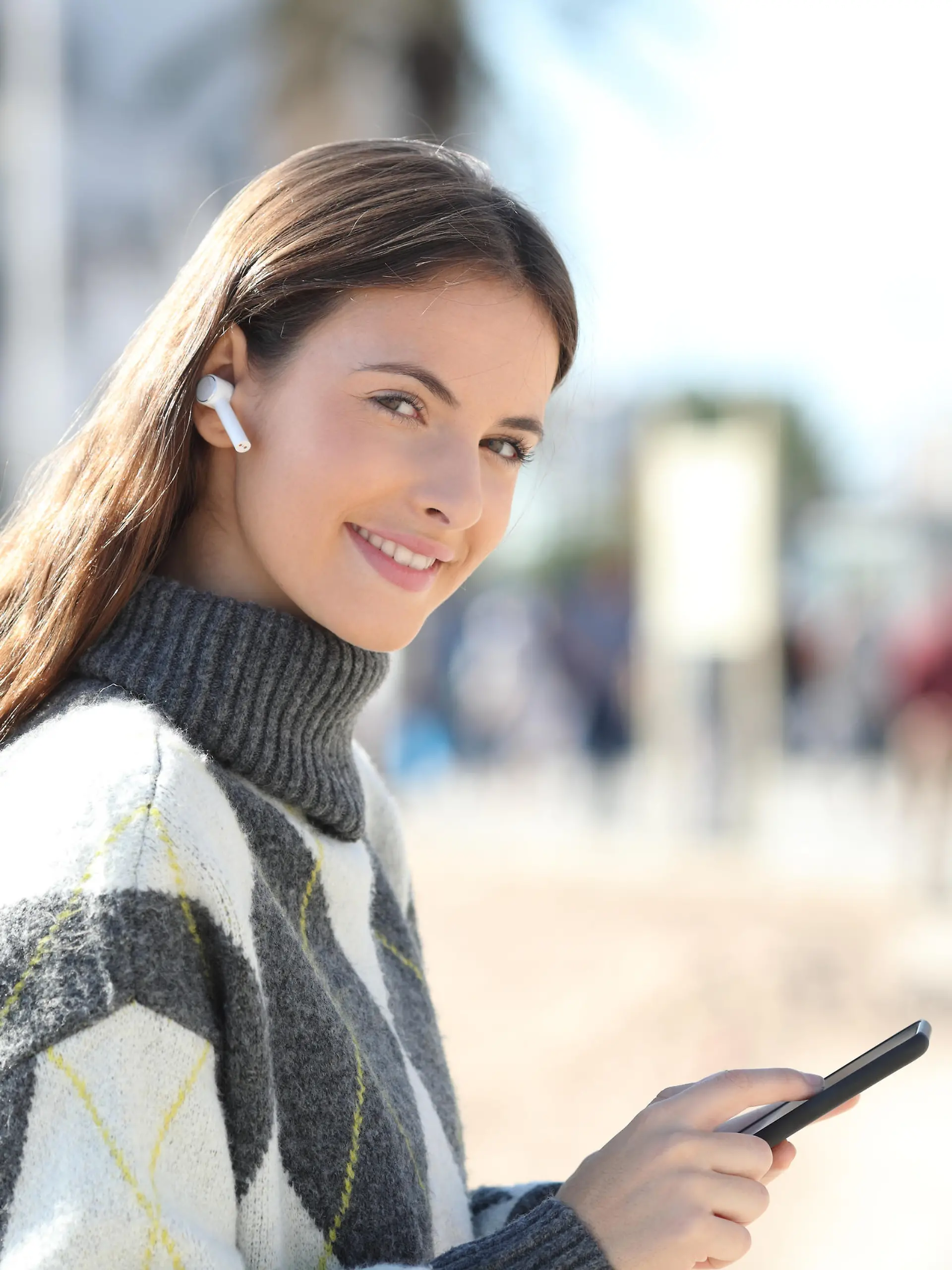 Happy girl holds phone listening to music looking at camera