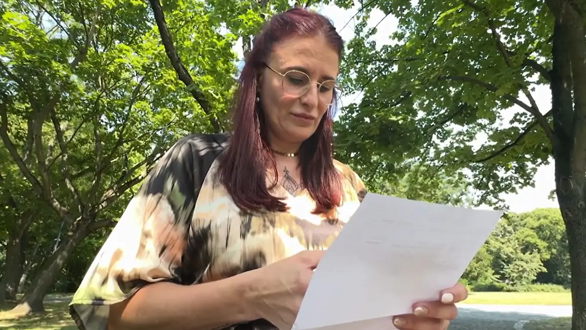 Eine Frau steht vor der Kamera und schaut auf ein Blatt Papier.