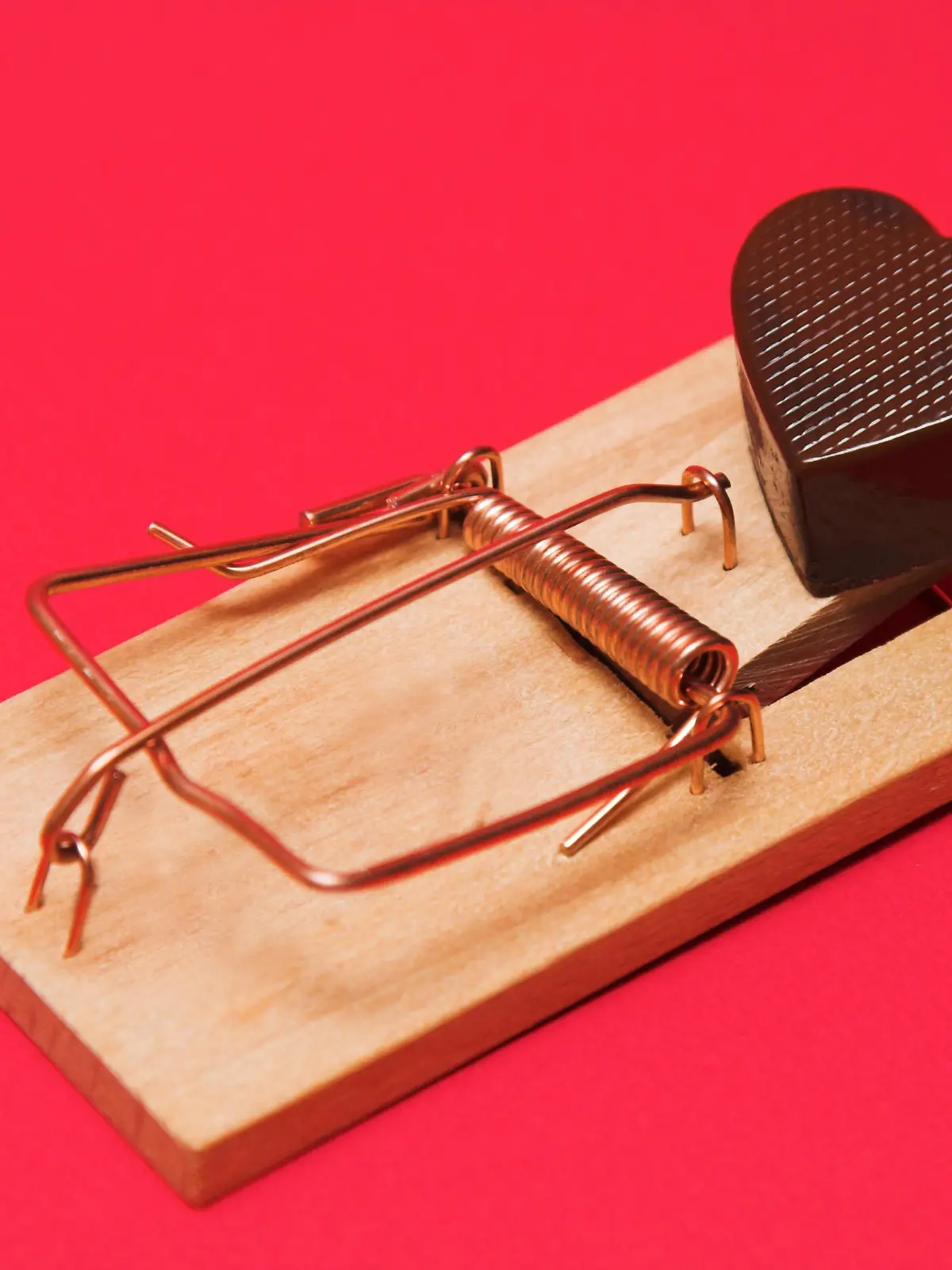 A mouse trap traping a candy shaped like a heart.