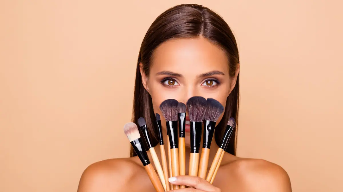 Close up portrait of brunette hair leisure lifestyle good-looking lovely pretty lady with her make up brushes shoulders she look at camera hide face isolated on pastel beige background