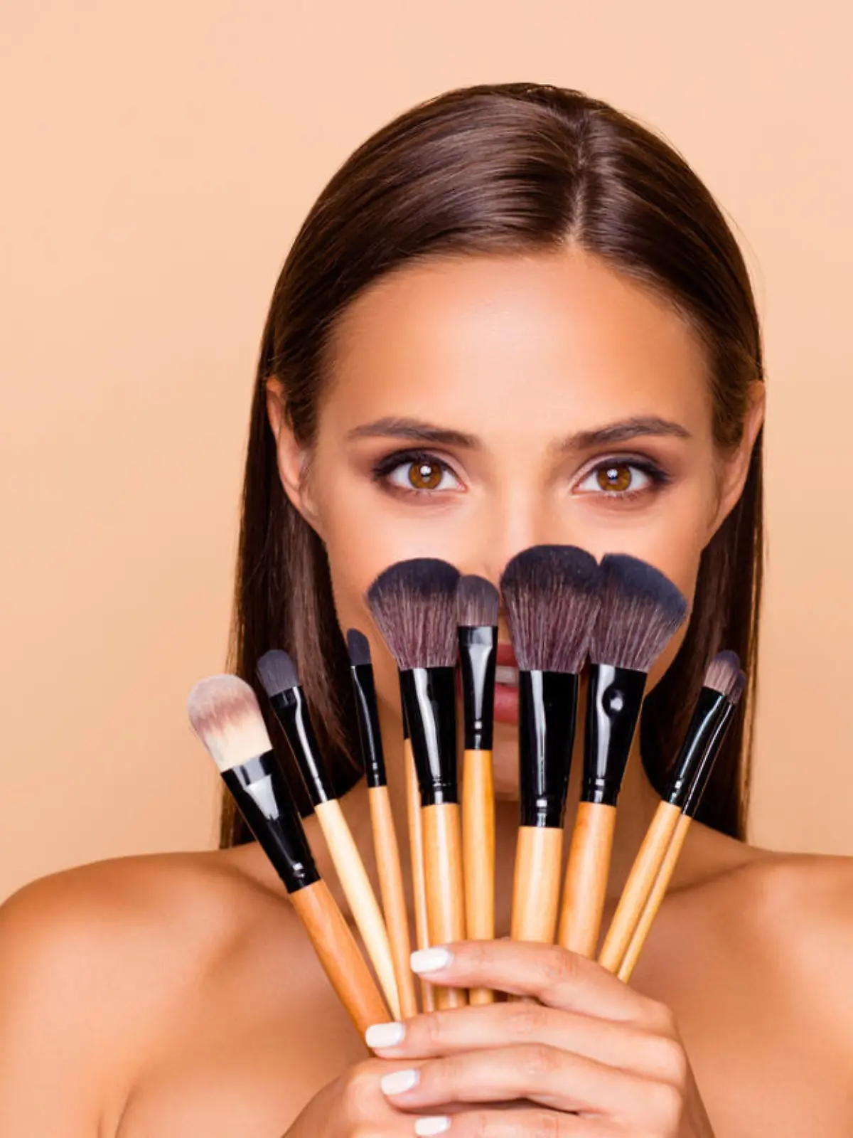 Close up portrait of brunette hair leisure lifestyle good-looking lovely pretty lady with her make up brushes shoulders she look at camera hide face isolated on pastel beige background