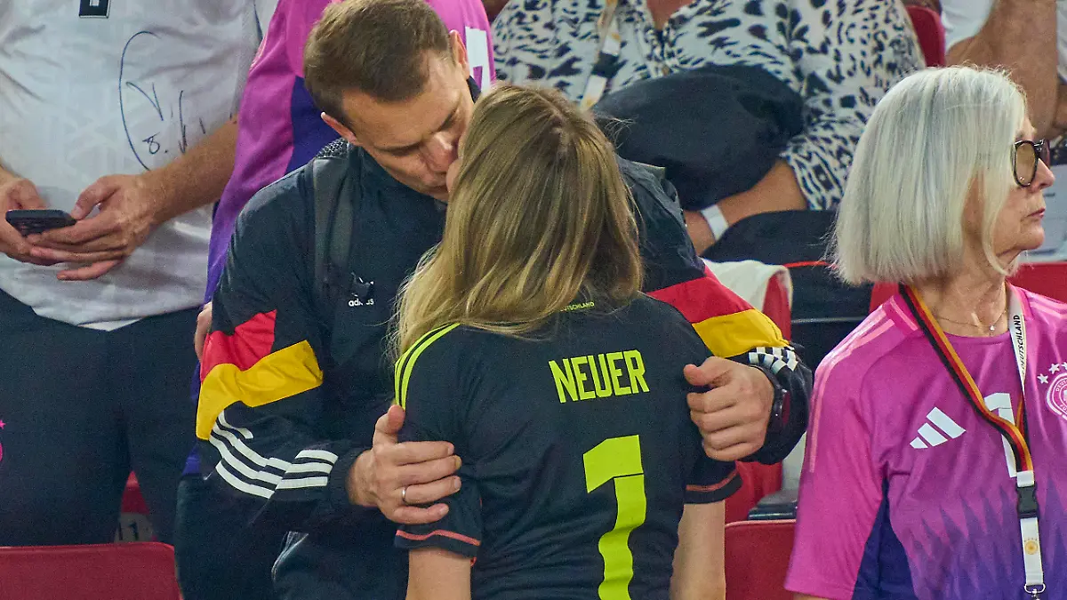 Manuel Neuer und seine Ehefrau Anika küssen sich auf der Tribüne eines Fußballstadions.