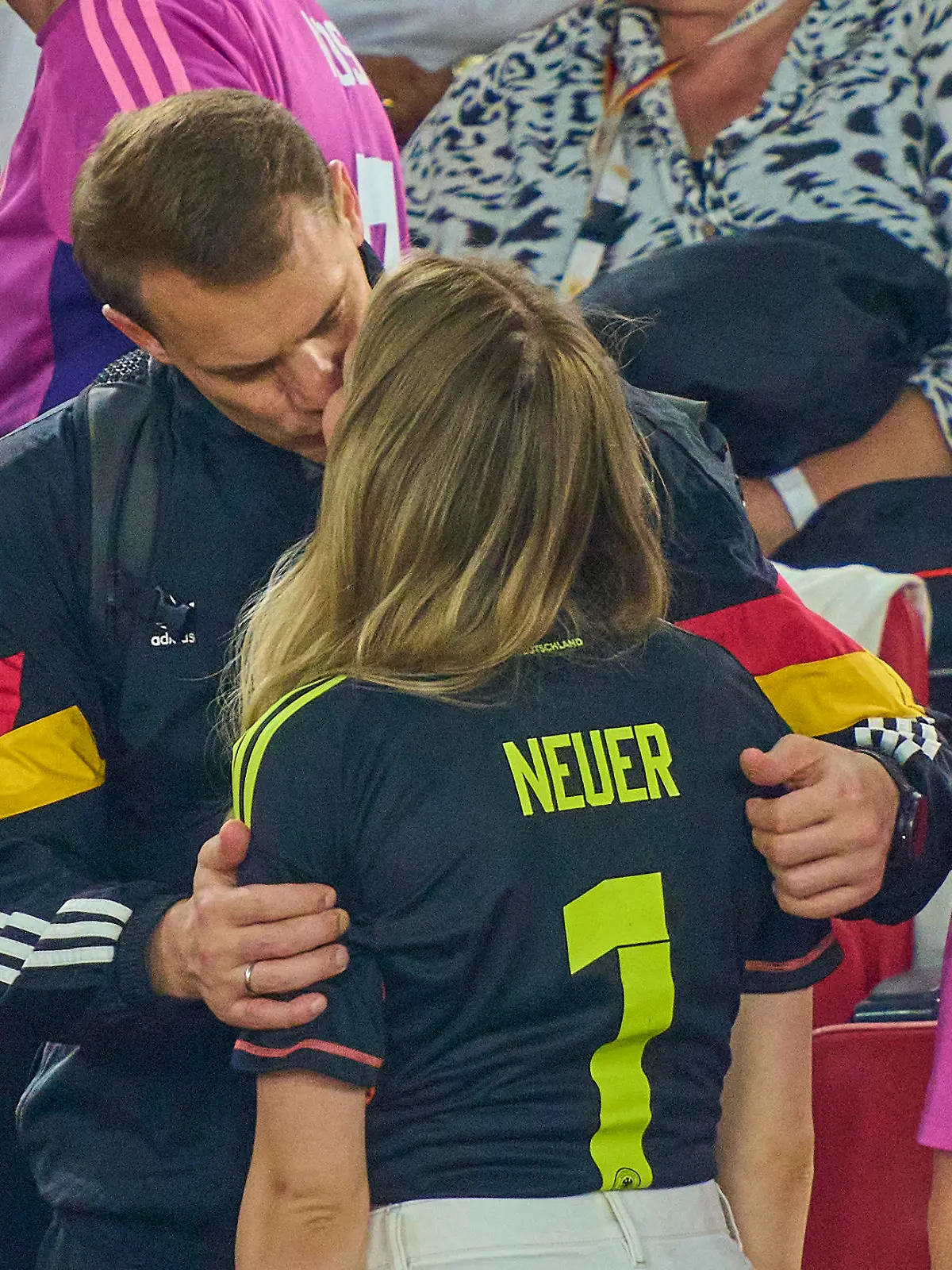 Manuel Neuer und seine Ehefrau Anika küssen sich auf der Tribüne eines Fußballstadions.