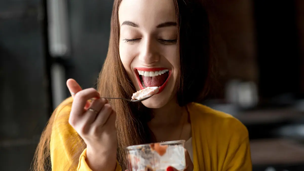 Young smiling woman dressed in yellow sweater eating ice cream in the dark cafe interior