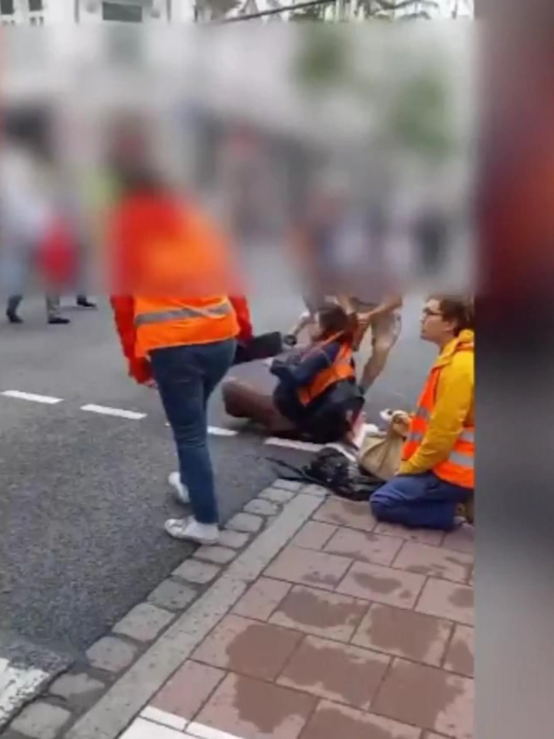 Zwei Passanten werden dabei gefilmt, wie sie anhaltend Klimakleber von der Straße zerren. Diese setzen sich immer wieder zurück auf den Asphalt. Offenbar setzt einer der Passanten derartige Kraft ein, dass ein Aktivist ruft "ich kriege keine Luft".