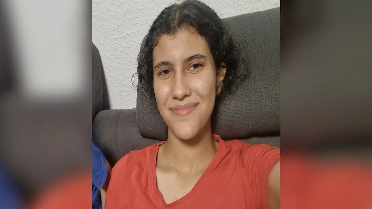 Ein Mädchen mit braunen Haaren und rotem T-Shirt macht ein Selfie auf einer Couch.