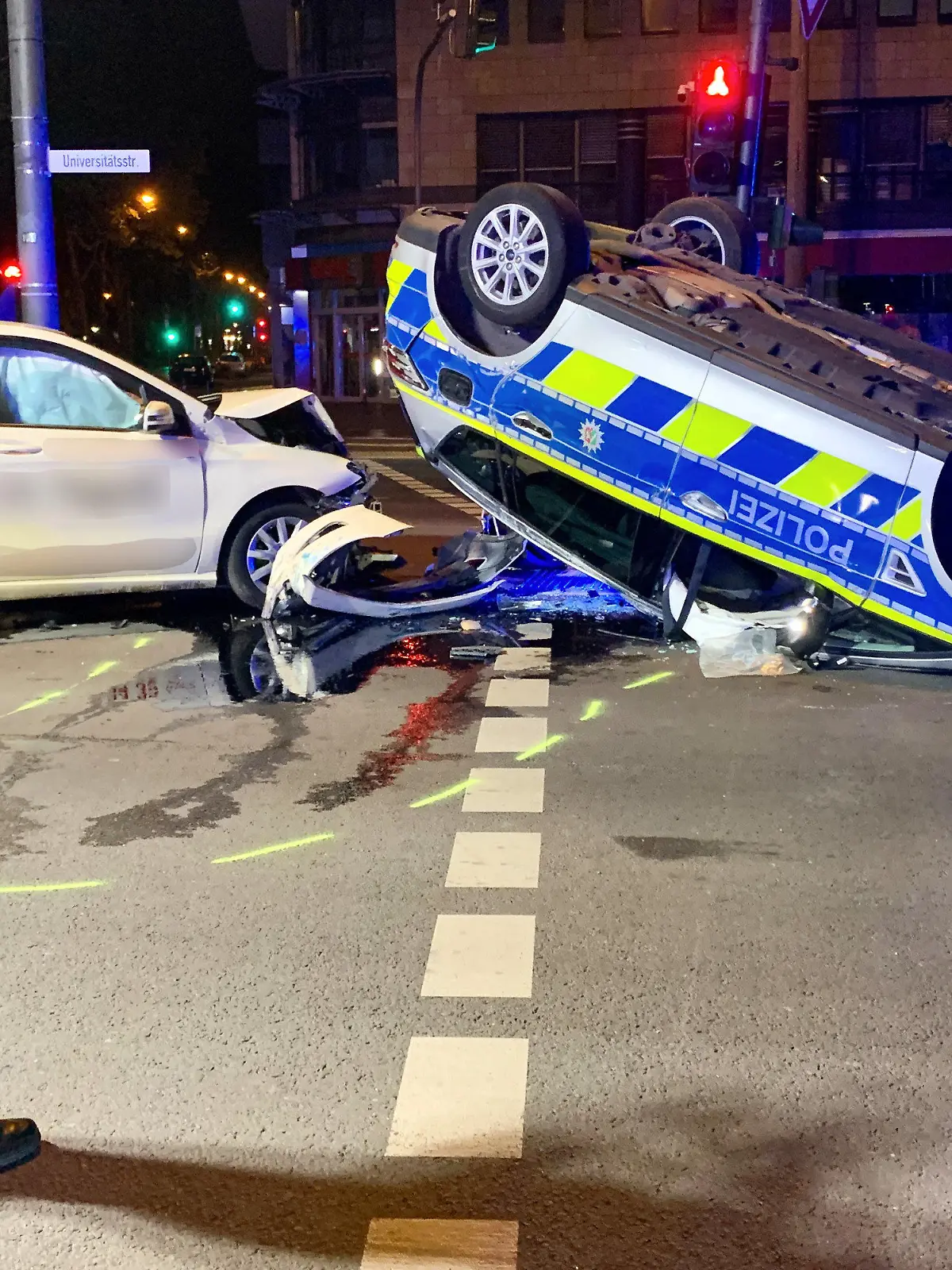 07.05.2022, Nordrhein-Westfalen, Köln: Eine polizistin betrachtet die Unfallstelle. Auf dem Weg zu einem Einsatz ist ein Streifenwagen in Köln in der Nacht auf Samstag mit einem Taxi kollidiert  - dabei sind sechs Menschen verletzt worden. Wie ein Sprecher der Polizei mitteilte, waren zwei Beamte ursprünglich zu einer Schlägerei gerufen worden und bogen mit ihrem Wagen links ab, als ihnen ein Taxi entgegenkam. Der Taxifahrer konnte wohl nicht mehr rechtzeitig bremsen und fuhr seitlich in den Streifenwagen. Dieser überschlug sich und blieb auf dem Dach liegen. Foto: Daniel Evers/WupperVideo/dpa +++ dpa-Bildfunk +++