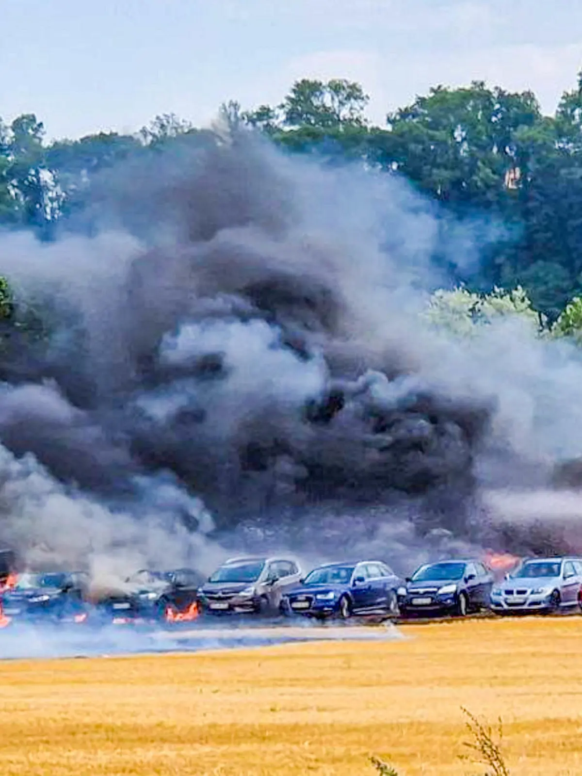 02.07.2023, Baden-Württemberg, Bad Wimpfen: Einsatzkräfte der Feuerwehr löschen auf einem Behelfsparkplatz ein Feuer. Mindestens zwölf Autos seien bei dem Brand am Sonntag durch Flammen und Hitze beschädigt worden, einige davon auch schwer. Foto: ER24/EinsatzReport24/dpa +++ dpa-Bildfunk +++