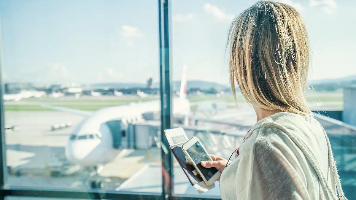 Young woman in airport waiting for flight sitting on bench with phone and passport in hands