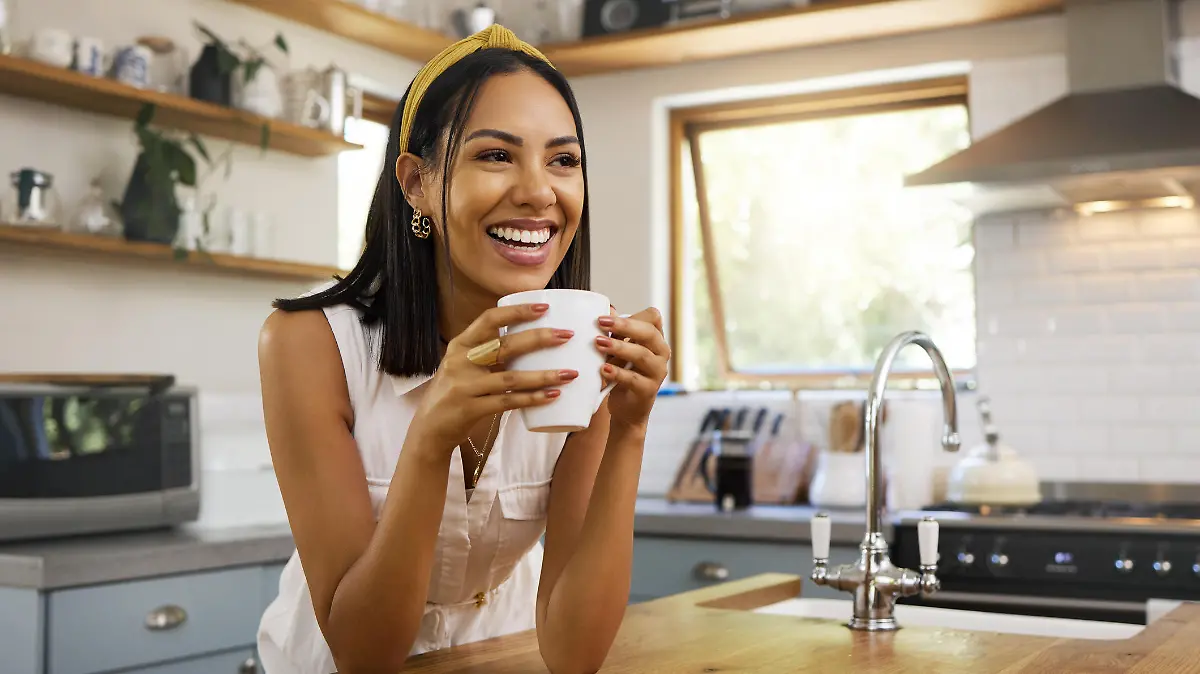 Happy woman, coffee or tea in home kitchen and relax with a smile in the morning at house. Calm young person, smiling at peace and caffeine drink to wake up to start day with positive productive vibe