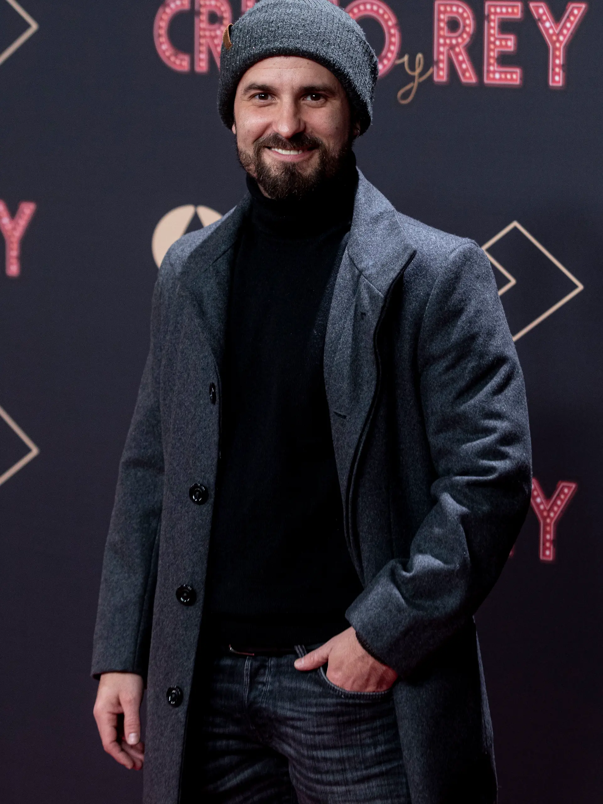 Schauspieler Julián Ortega trägt eine Wollmütze und einen grauen Anzug vor einer Werbewand. Der Schauspieler starb überraschend im August 2024. 