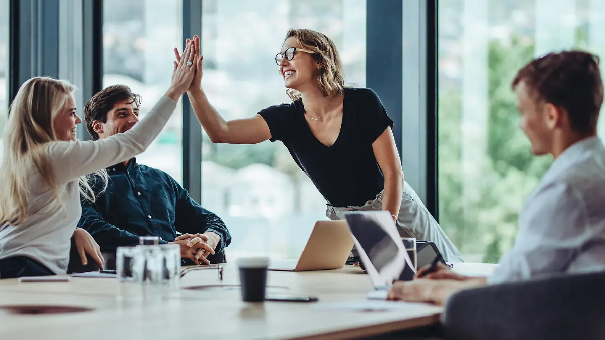 Female professional giving a high five to her colleague in conference room. Group of colleagues celebrating success in a meeting.