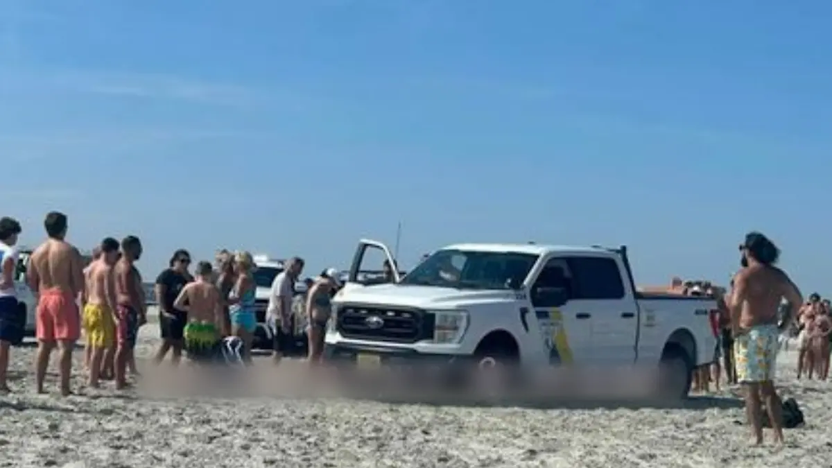 Menschen stehen um einen Pickup-Truck am Strand.