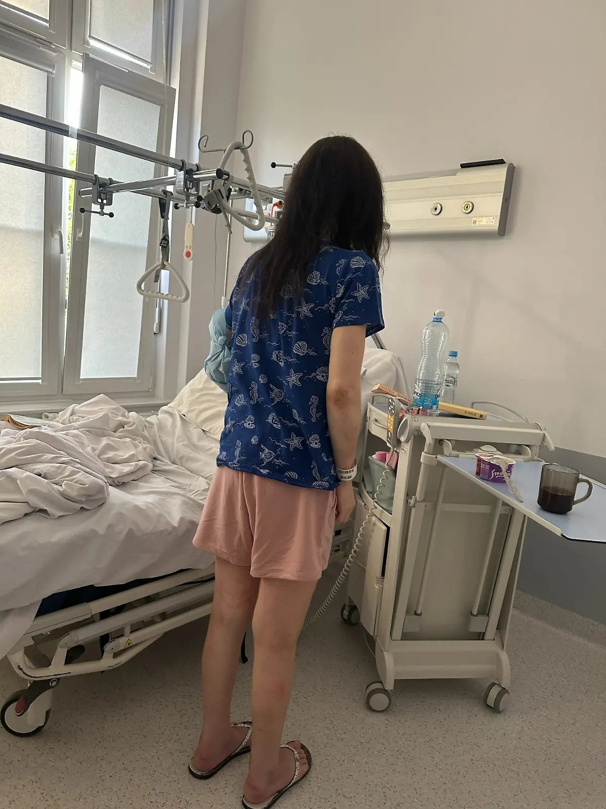Eine Frau steht vor einem Krankenbett.