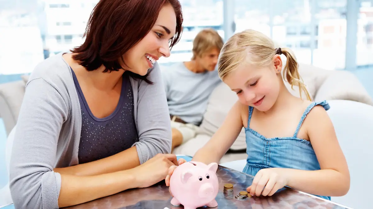 Pretty little girl putting money in piggy bank with her parents in the living room
