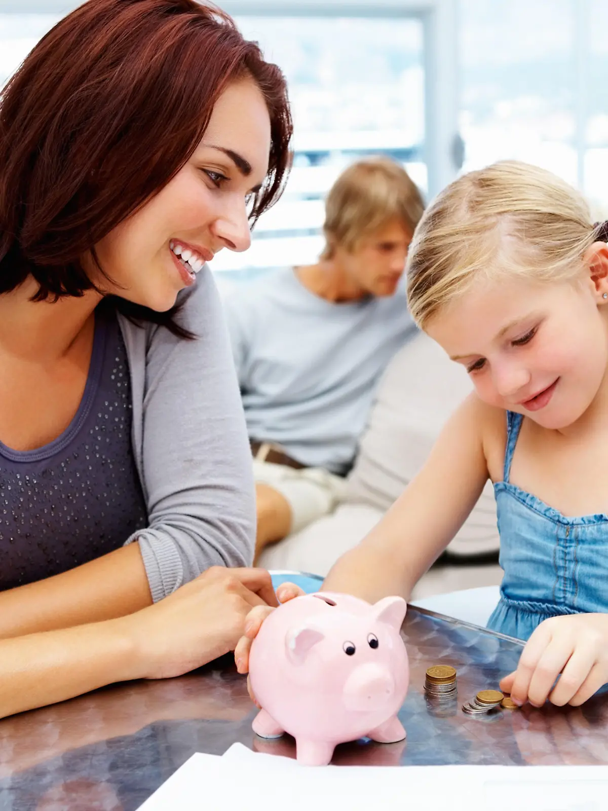 Pretty little girl putting money in piggy bank with her parents in the living room