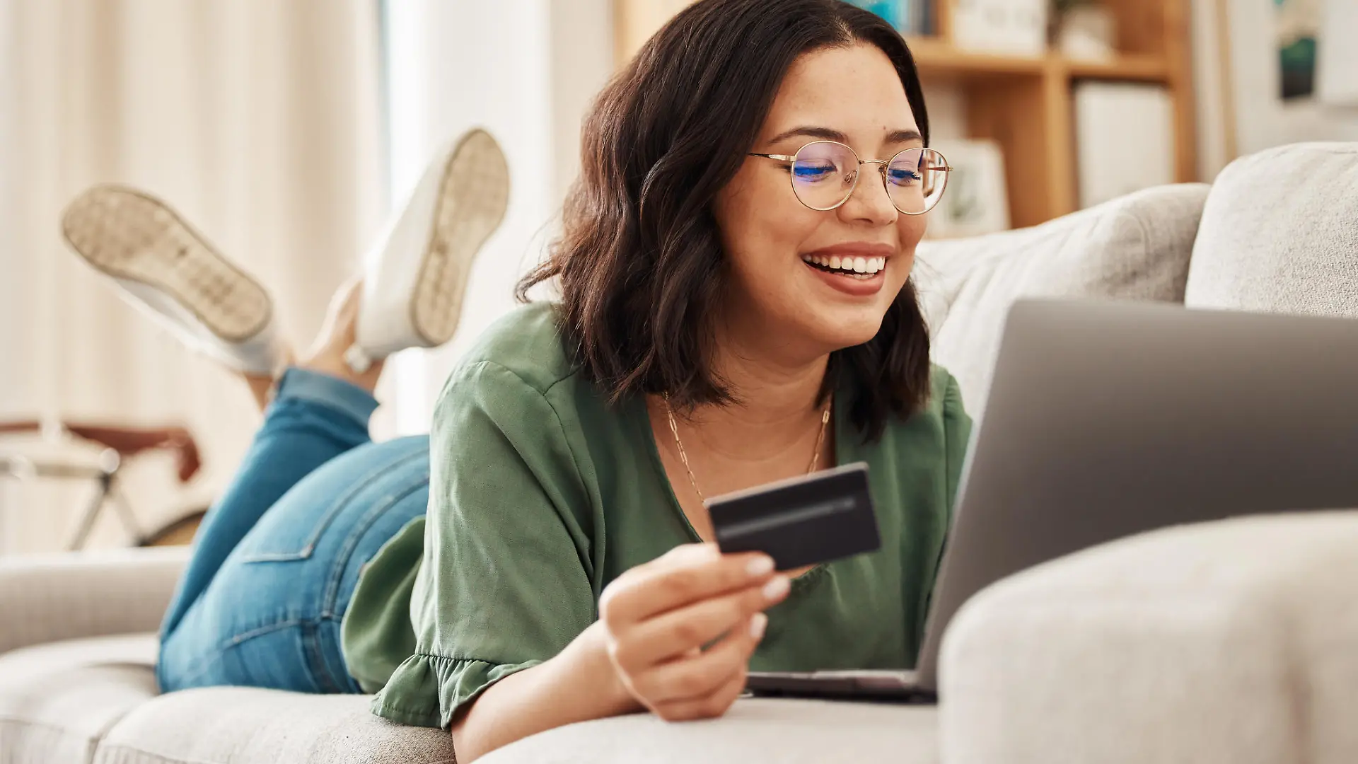 Relax, laptop and credit card, happy woman on couch in living room for internet banking in home for online shopping. Ecommerce payment, smile and cashback, girl on sofa with computer and website sale