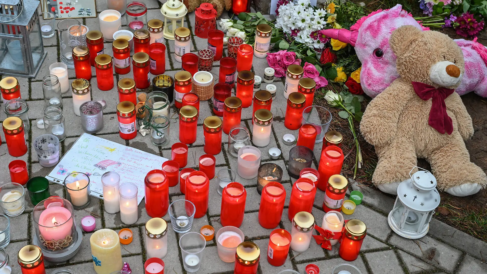 06.12.2021, Brandenburg, Senzig: Viele Kerzen brennen vor auf einem Gehweg vor einem Einfamilienhaus in einem Ortsteil der Stadt Königs Wusterhausen im Landkreis Dahme-Spreewald. Am 04.12.2021 hatten Zeugen in diesem Einfamilienhaus leblose Personen gesehen und die Polizei alarmiert. Die Beamten fanden die fünf Bewohner des Hauses tot vor. Darunter waren auch drei Kinder im Alter von 4, 8 und 10 Jahren, wie die Staatsanwaltschaft Cottbus und die Polizeidirektion Süd in einer gemeinsam Presseerklärung mitteilten. Die beiden Erwachsenen seien 40 Jahre alt gewesen. Foto: Patrick Pleul/dpa-Zentralbild/dpa - ACHTUNG: Namen wurden aus rechtlichen Gründen gepixelt +++ dpa-Bildfunk +++