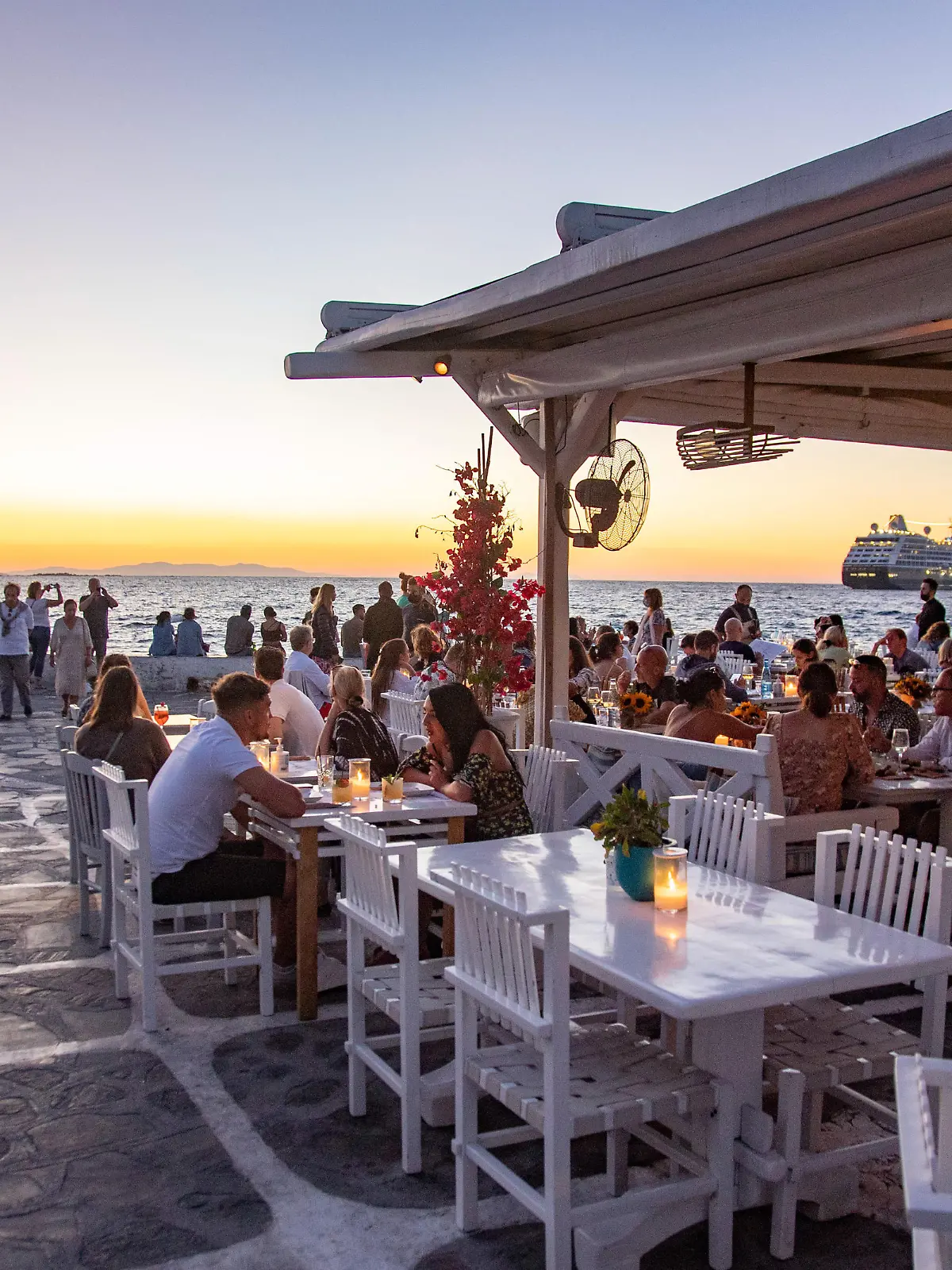People enjoy the sunset from Little Venice. Little Venice in Mykonos island during the magic hour of the sunset. Tourists enjoy a drink at the terrace or balcony of the whitewashed cafe bars or dinner at a restaurant just above the water at the little waterfront area under the famous windmills of the island. The Greek island of Myconos is a popular glamorous Mediterranean travel destination for holidays in the Cyclades, the Aegean Sea with the iconic whitewashed buildings, the sandy beaches and famous parties at the beach bars. The tourism and travel industry had a negative impact on the business and local economy sector due to the Covid-19 Coronavirus pandemic. Mykonos island, Greece on October 10, 2021 (Photo by Nicolas Economou/NurPhoto)