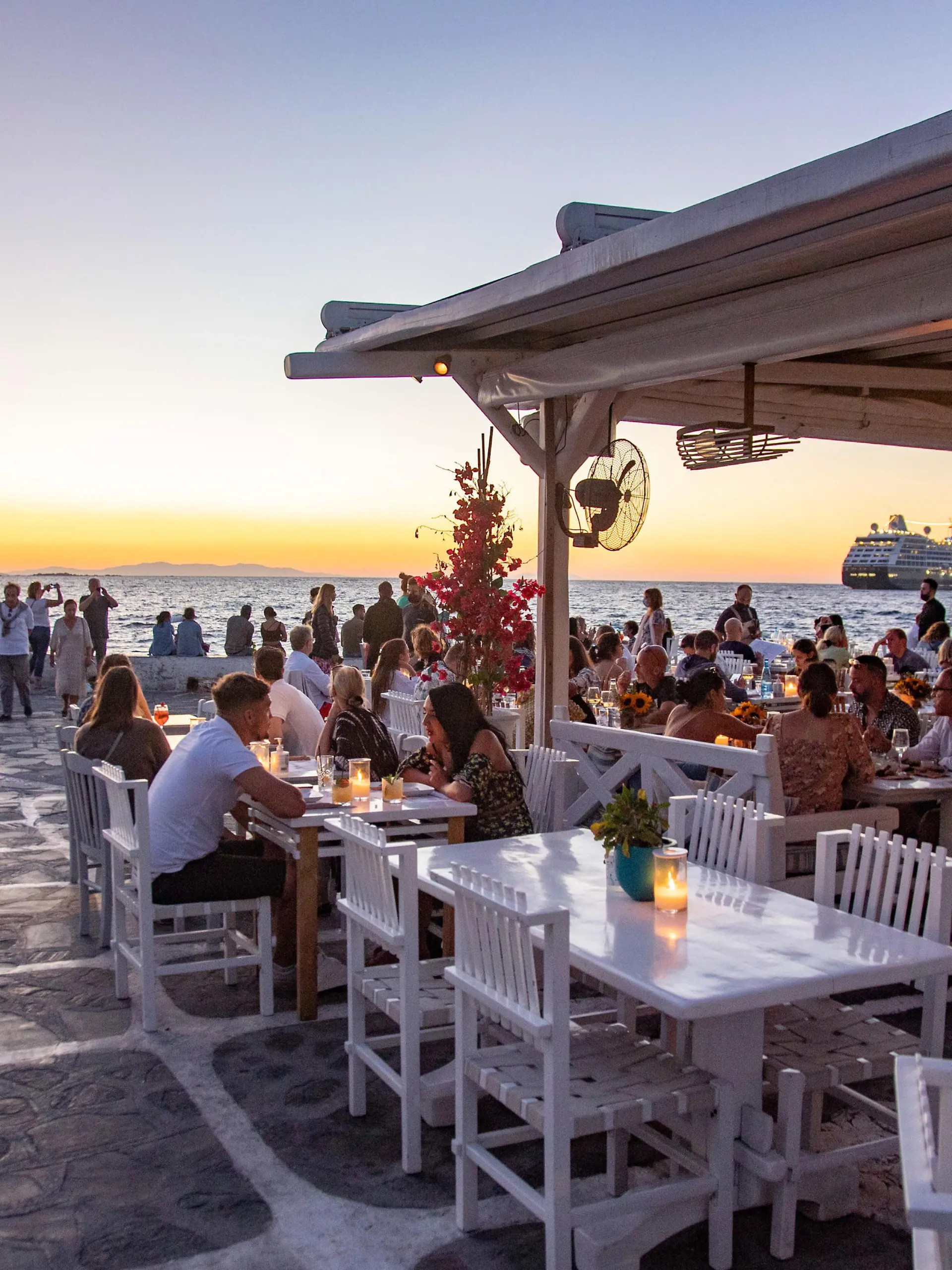 People enjoy the sunset from Little Venice. Little Venice in Mykonos island during the magic hour of the sunset. Tourists enjoy a drink at the terrace or balcony of the whitewashed cafe bars or dinner at a restaurant just above the water at the little waterfront area under the famous windmills of the island. The Greek island of Myconos is a popular glamorous Mediterranean travel destination for holidays in the Cyclades, the Aegean Sea with the iconic whitewashed buildings, the sandy beaches and famous parties at the beach bars. The tourism and travel industry had a negative impact on the business and local economy sector due to the Covid-19 Coronavirus pandemic. Mykonos island, Greece on October 10, 2021 (Photo by Nicolas Economou/NurPhoto)
