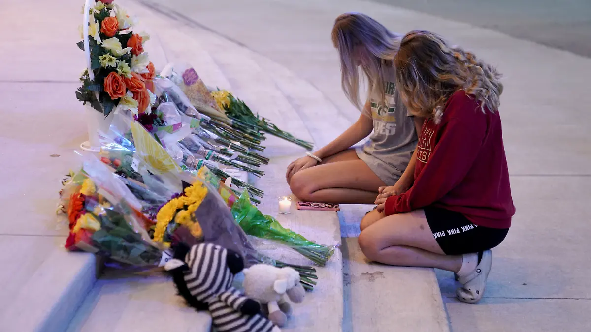 Zwei Schülerinnen knien trauernd vor der Schule, sie haben Blumen niedergelegt.