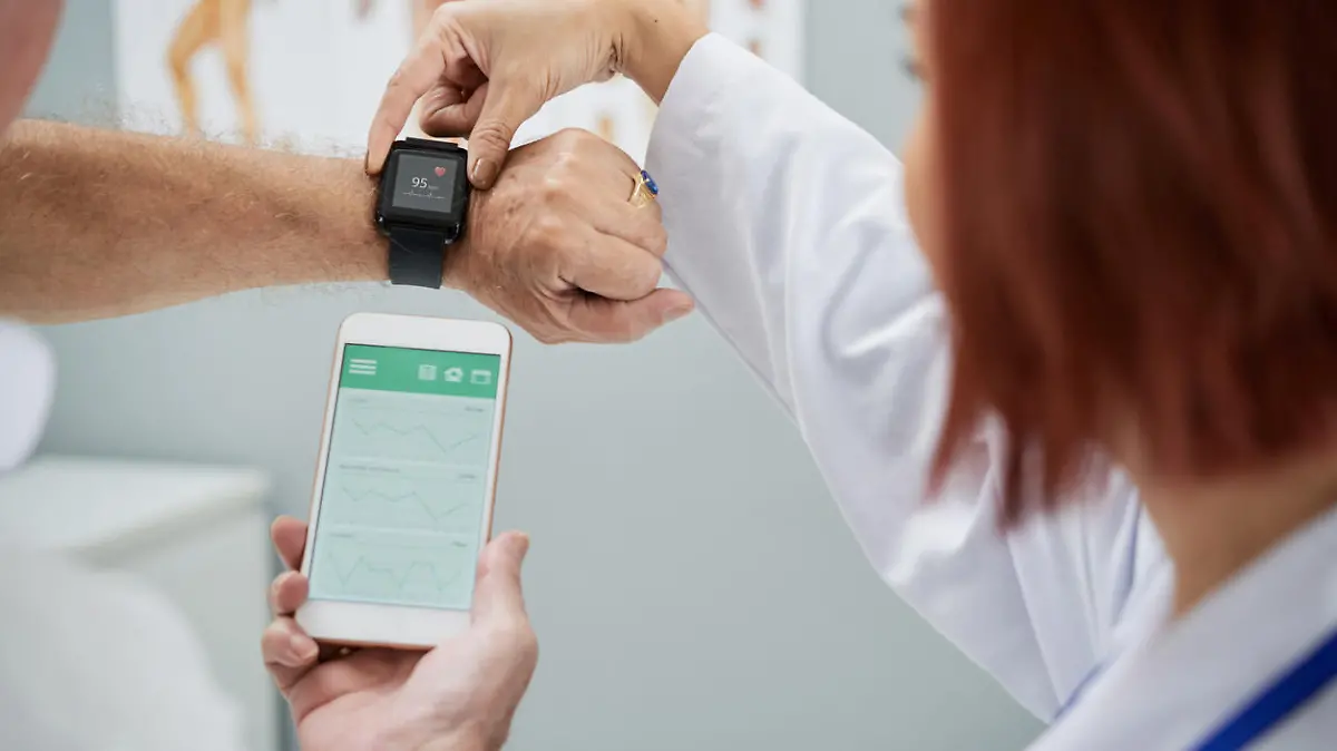 Doctor showing senior patient how to synchronize health app in smartphone and smartwatch