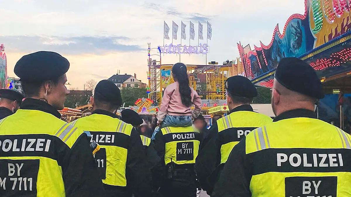 Bild auf den Frühlingswiesn in München: Ein Mädchen sitzt auf den Schultern eines Polizisten, drum herum weitere Beamte