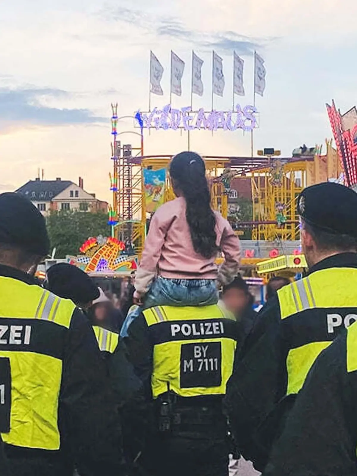 Bild auf den Frühlingswiesn in München: Ein Mädchen sitzt auf den Schultern eines Polizisten, drum herum weitere Beamte