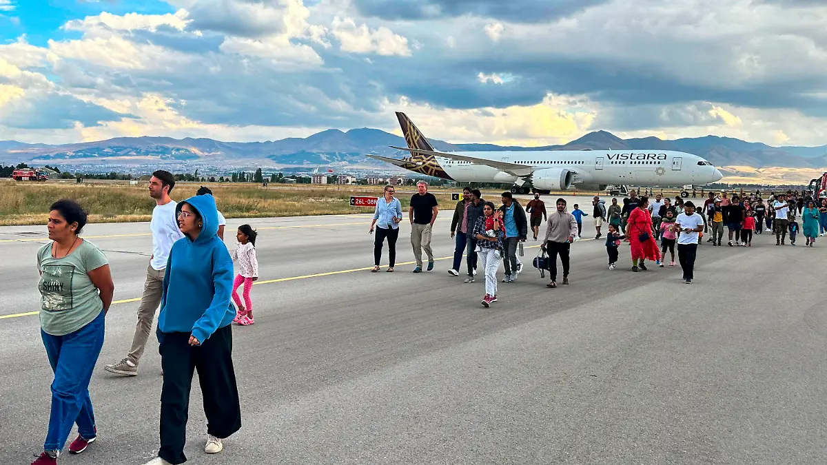 Passagiere auf einem Rollfeld, dahinter ein Flugzeug. 