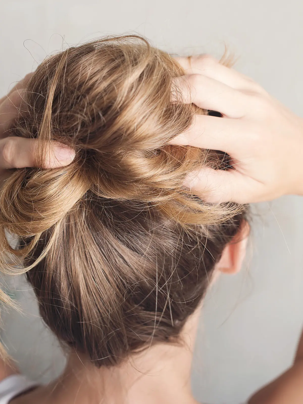 Beautiful young woman is styling hair in bathroom at home