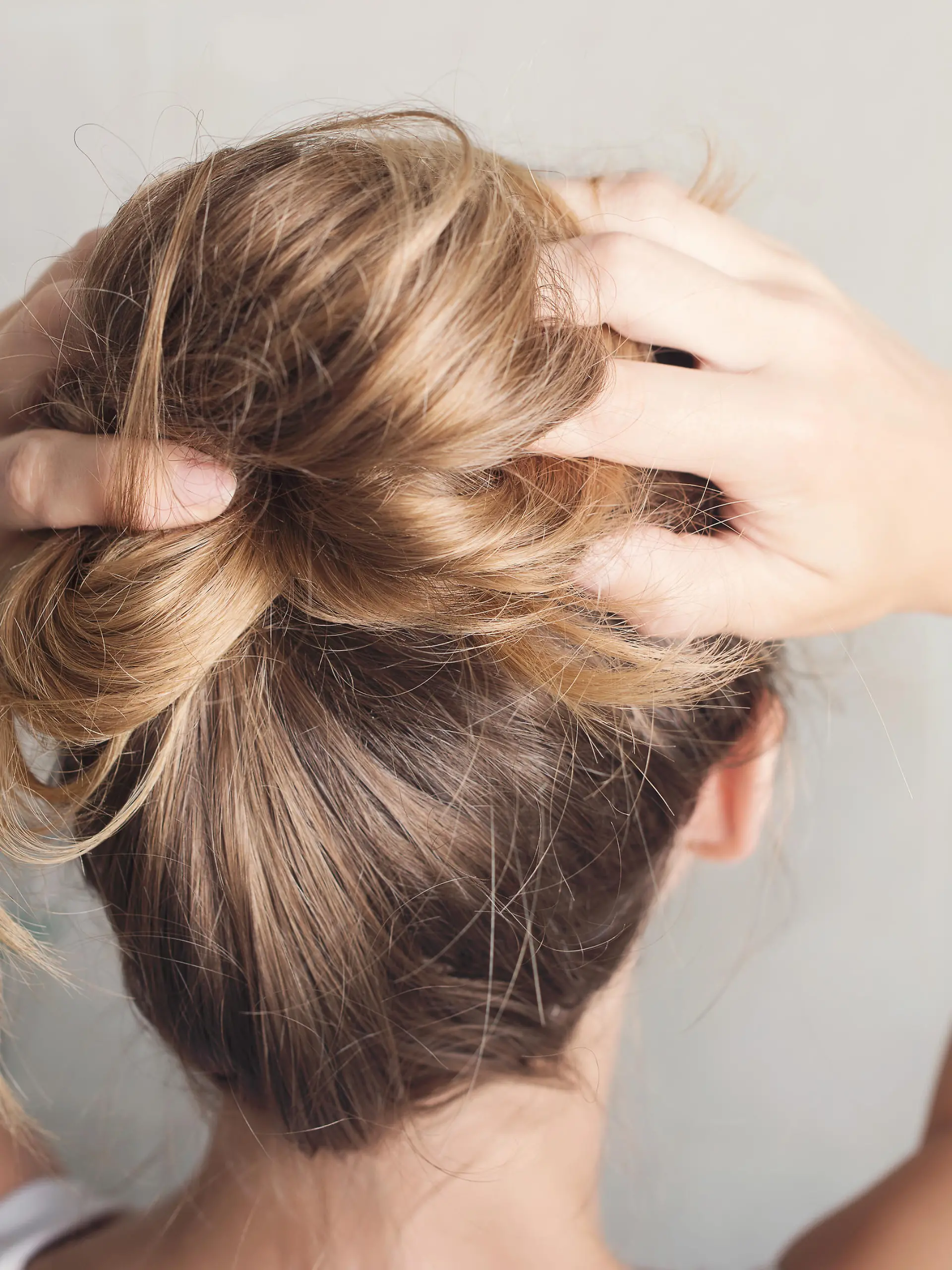 Beautiful young woman is styling hair in bathroom at home