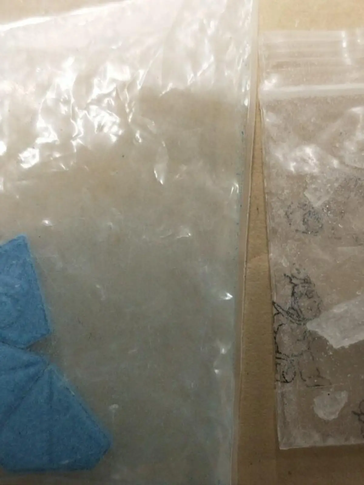 Zwei durchsichtige Druckverschlusstütchen mit blauen Ecstasy Pillen der Sorte "Blue Punisher". Daneben ein weiteres Tütchen mit Kristallen - vermutlich Crystal Meth.