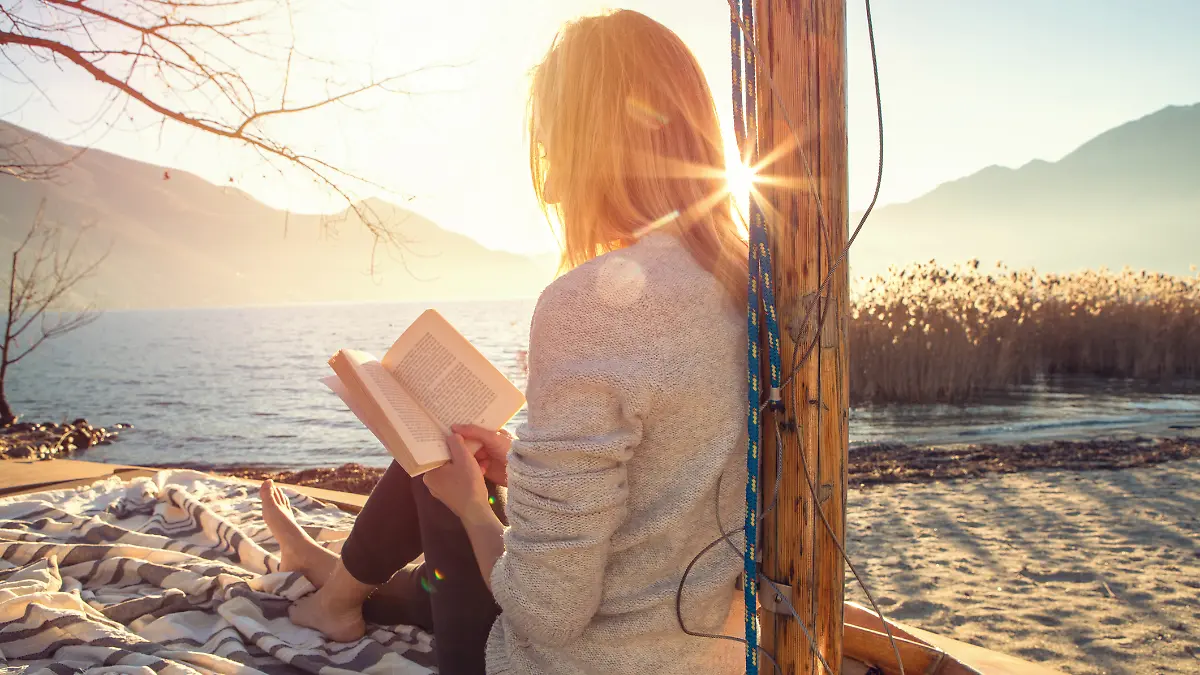 Frau liest Buch mit Sonne im Hintergrund.