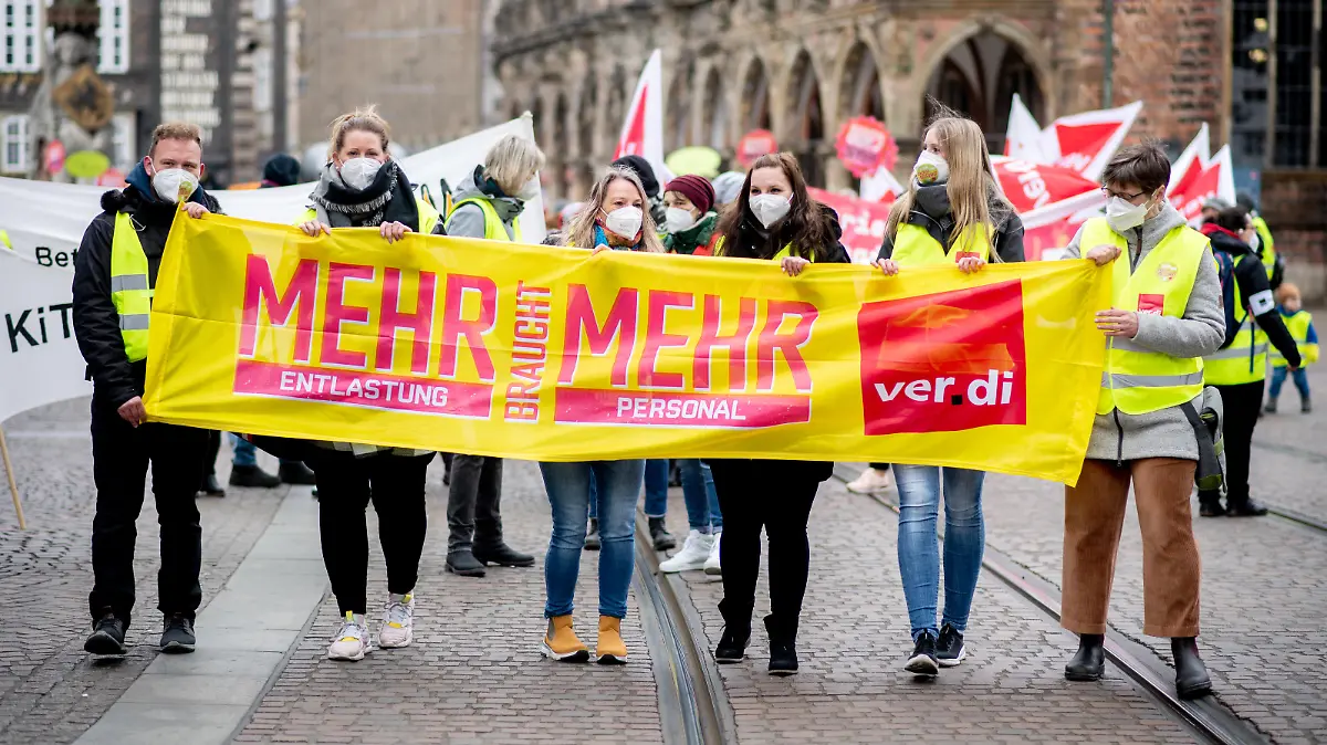 Mitarbeiterinnen und Mitarbeiter kommunaler Kitas und sozialer Dienste gehen während einer Kundgebung mit einem Transparent mit der Aufschrift „Mehr braucht mehr“ über den Marktplatz. Zahlreiche Beschäftigte der kommunalen Kitas und sozialer Dienste in Niedersachsen und Bremen haben die Arbeit niedergelegt. Sie folgten dem Aufruf der Gewerkschaft Verdi zu einem ganztägigen Warnstreik, um in den laufenden Tarifverhandlungen Druck auf die Arbeitgeber auszuüben.