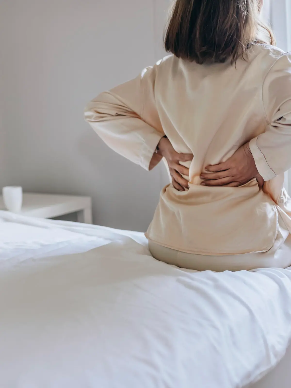Cropped Image of Senior Woman Suffering From Backache in Morning Sitting on Bed, Panorama With Free Space. Lower Back Pain in Elderly Person. Woman Feels Back Pain Massaging Aching Muscles. Mature Woman Feeling Morning Discomfort in Aching Back in the Bedroom.