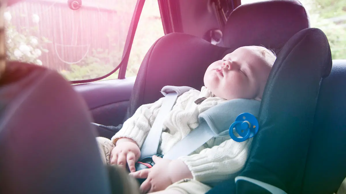 Little boys has fallen asleep during a road trip. He sit securely in a baby car seat and wears a seat belt.