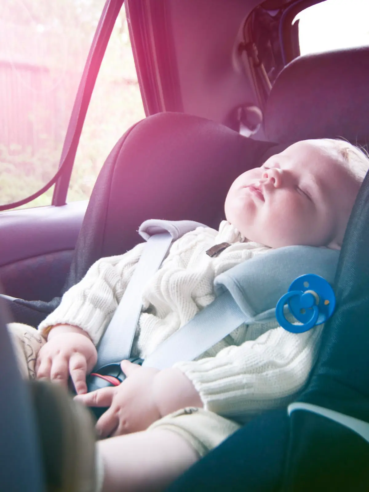 Little boys has fallen asleep during a road trip. He sit securely in a baby car seat and wears a seat belt.