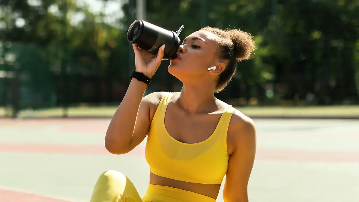 Frau in Sportkleidung trinkt aus einer Flasche