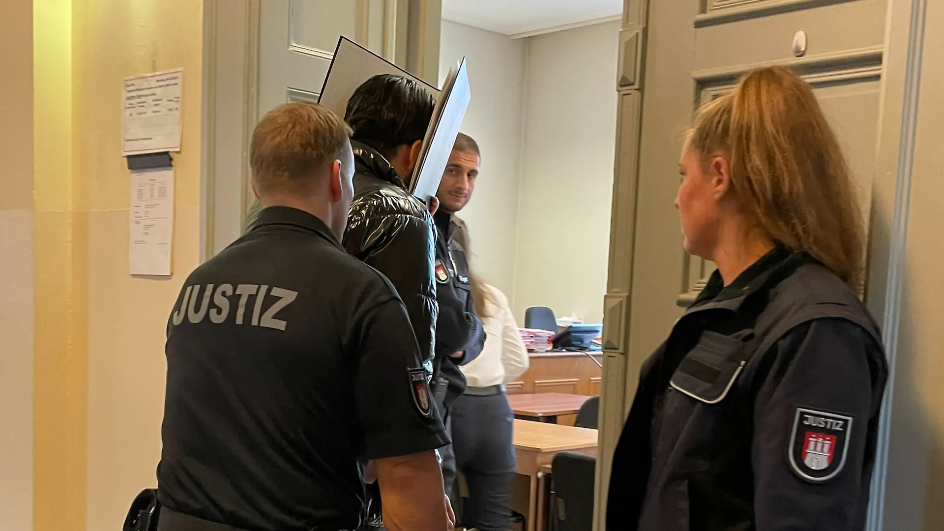 Versteckt hinter einem Aktenordner betritt der Angeklagte am ersten Prozesstag den Saal.