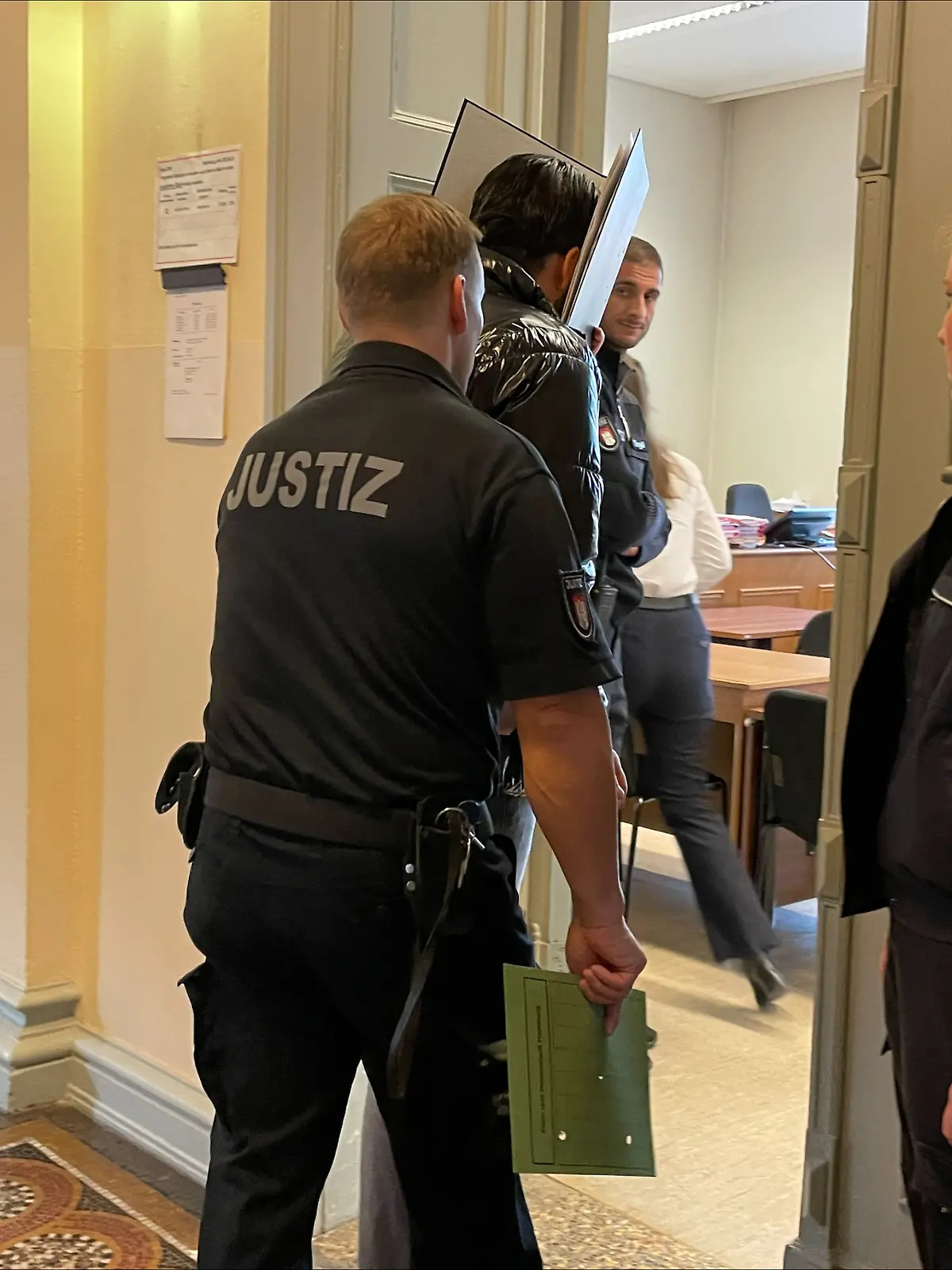 Versteckt hinter einem Aktenordner betritt der Angeklagte am ersten Prozesstag den Saal. 
