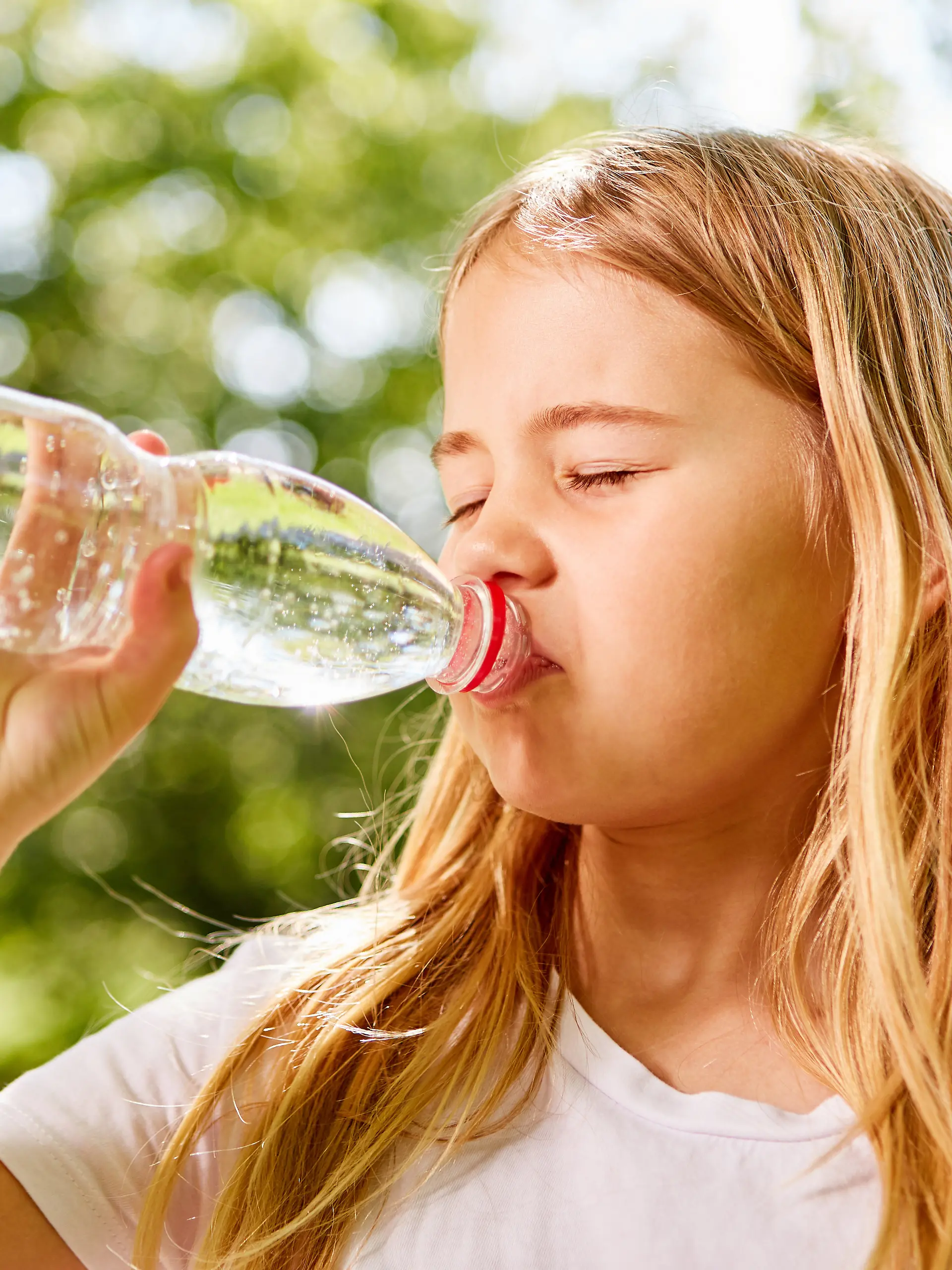 Ein Mädchen trinkt Wasser aus einer Plastikflasche. 