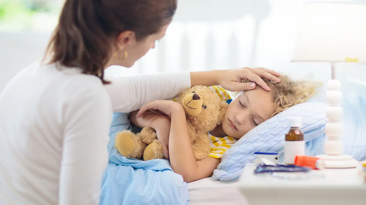 Kind liegt krank im Bett, Mutter streicht ihm über den Kopf