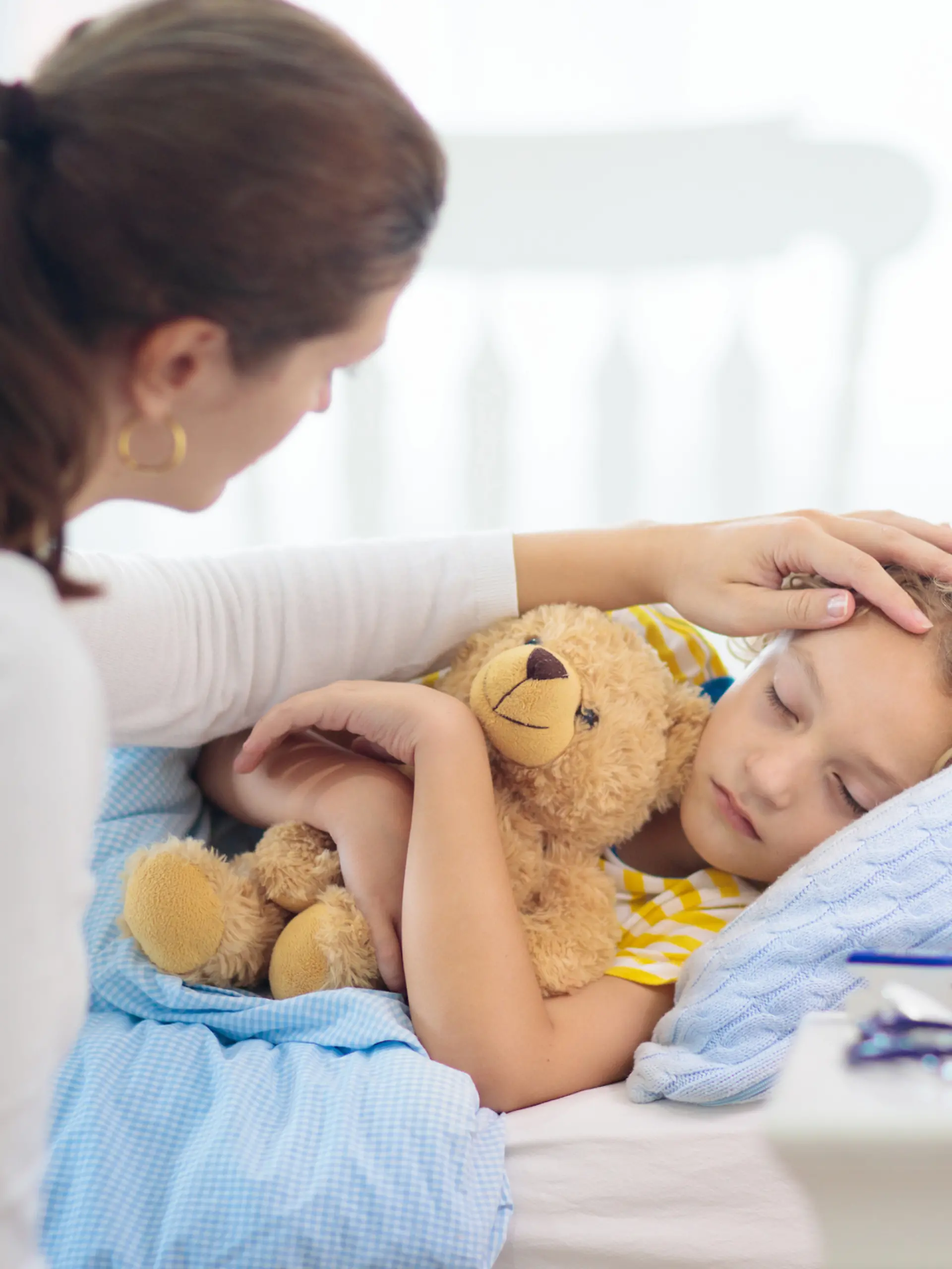 Kind liegt krank im Bett, Mutter streicht ihm über den Kopf