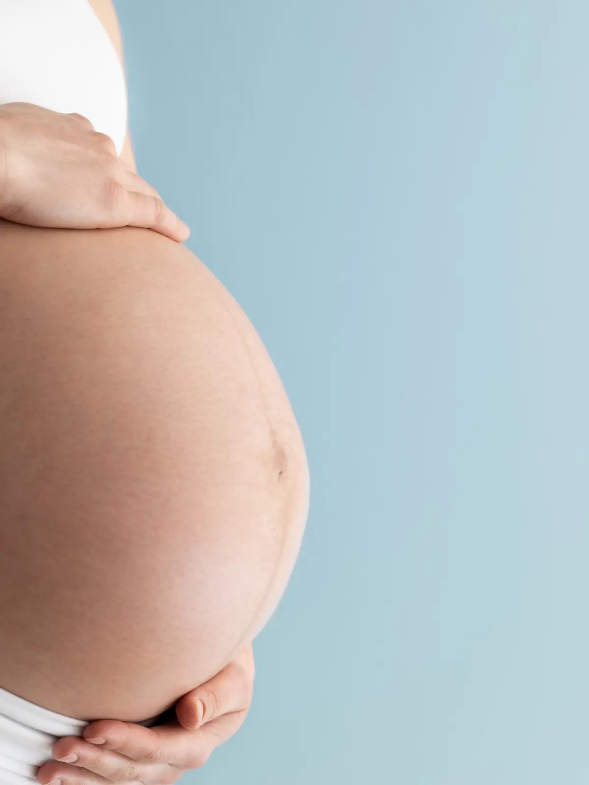 Eine Schwangere hält ihren nackten Schwangerschaftsbauch fest.
