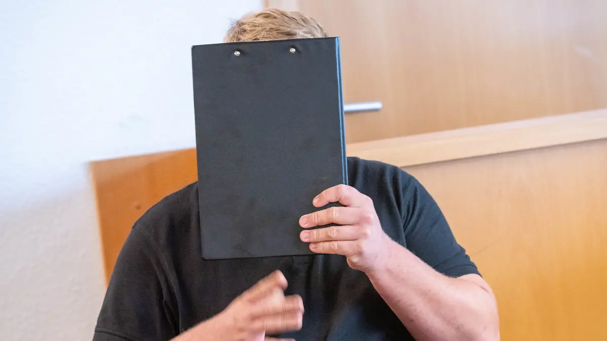 Der Angeklagte hält im Sitzungssaal im Amtsgericht einen Schreibblock vor sein Gesicht. Ein Jahr nach einem dramatischen Mähdrescherunfall in Hohen Luckow (Landkreis Rostock) muss sich ein 26-Jähriger wegen fahrlässiger Körperverletzung am Amtsgericht Rostock verantworten. Bei dem Angeklagten handelt es sich demnach um einen Kollegen des damals 25 Jahre alten Landwirts, der bei dem Unfall beide Beine verloren hatte.