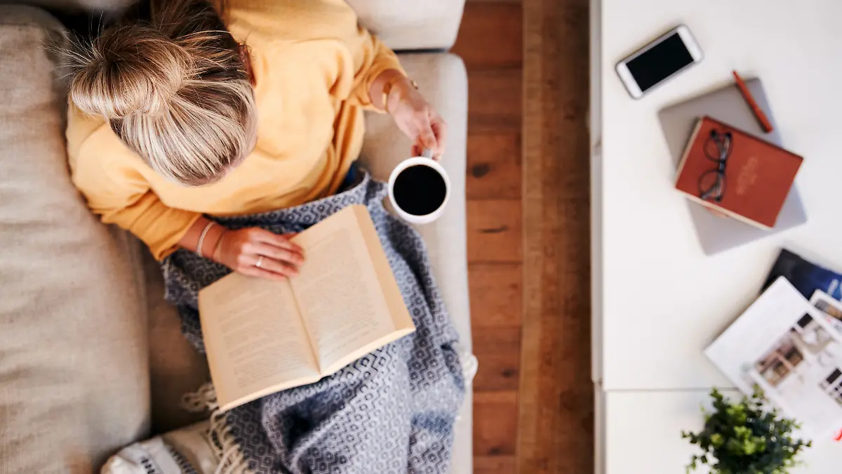 Frau trinkt Kaffee auf einer hellen Couch.